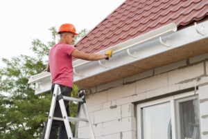 worker on a ladder installing gutter system on residential roof