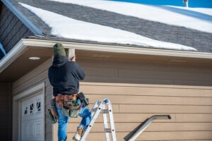 A roofing professional repairing a gutter for a house has snow on the roof.