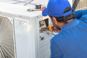An HVAC professional with a pair of pliers performing repair work on an HVAC unit. 