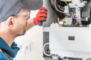 An HVAC technician looking at the inside of an HVAC to determine if there is an issue.