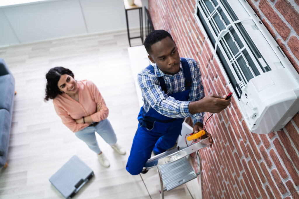 An HVAC technician inside of a home checking the electrical charge of a ductless mini split HVAC unit.