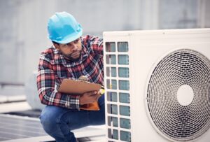 HVAC technician inspects unit holding a clipboard and wearing a plaid shirt.
