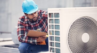 HVAC technician inspects unit holding a clipboard and wearing a plaid shirt.