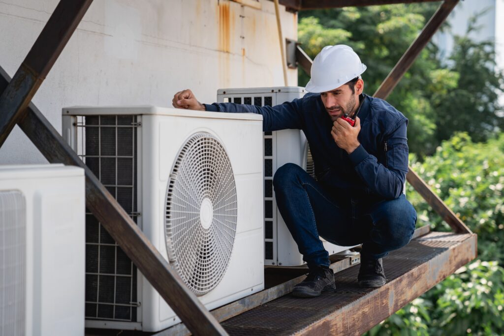 An HVAC technician inspecting an HVAC unit on top of a platform.