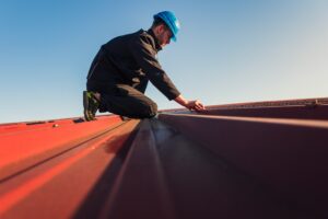 A roofing professional on top of a residential building knelt over repairing a roof.