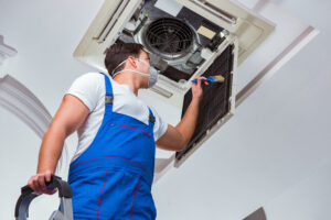 An HVAC technician with a mask on and other protective gear cleaning an HVAC system in preparation for a repair.