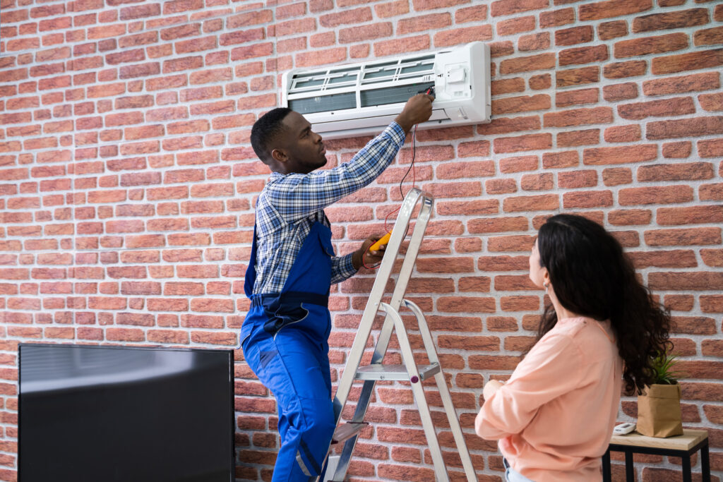 young woman observing as male hvac technician repairs mounted unit