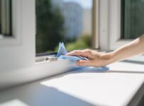 female hand with blue rag cleaning windowsill