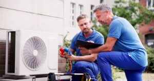 two hvac technicians wearing blue installing a unit