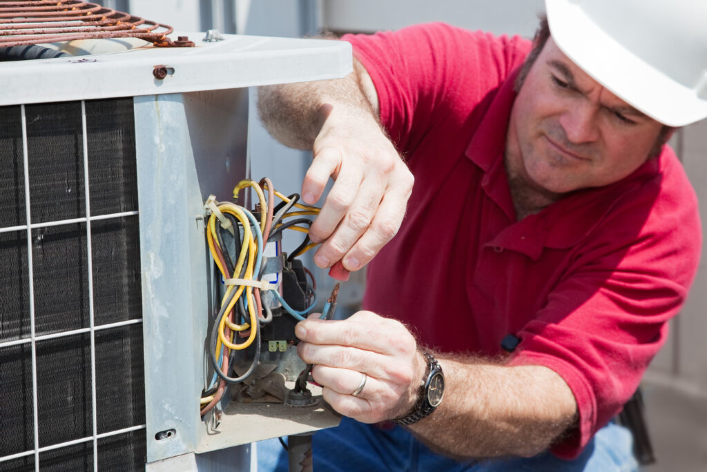 hvac technician repairing a unit in a red shirt