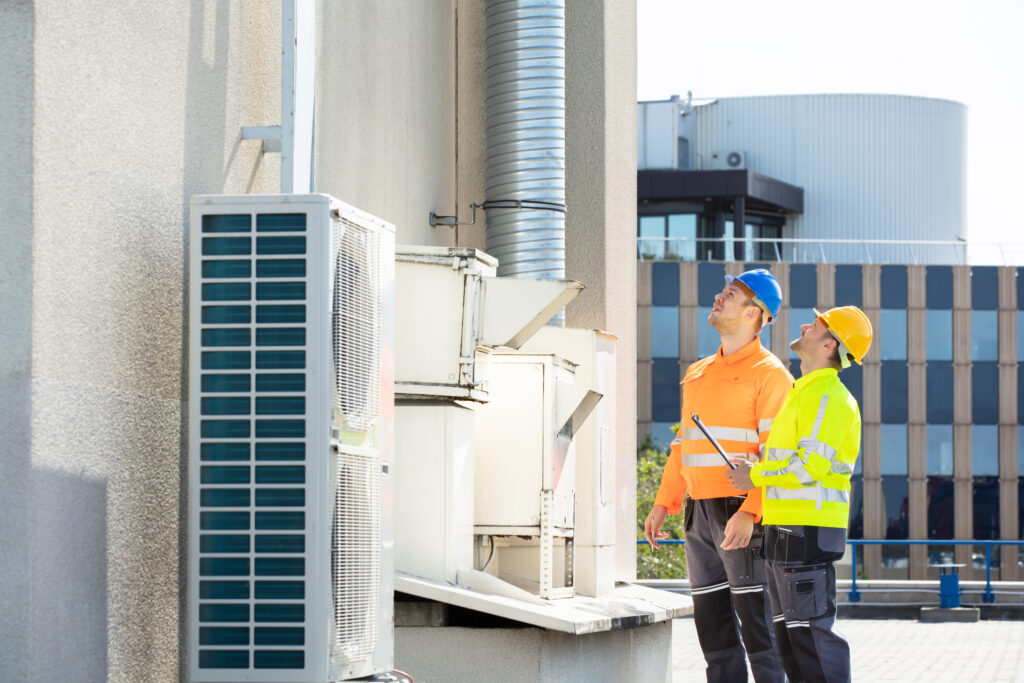 two technicians wearing safety jackets checking on hvac unit