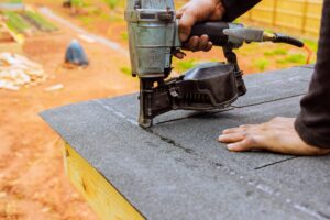 roofer using nail gun installs new asphalt