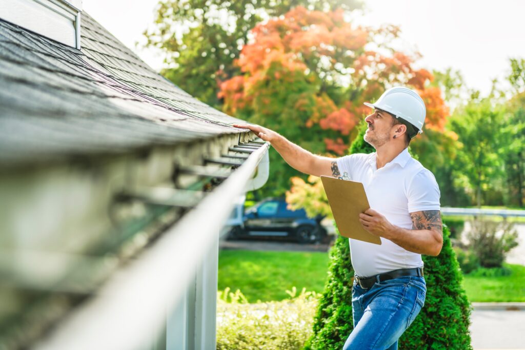 man with a white hard hat holding a whiteboard and looking at roof