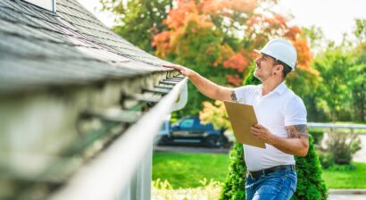 man with a white hard hat holding a whiteboard and looking at roof