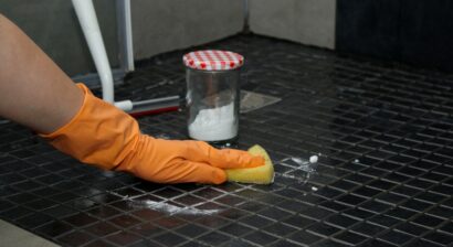 close up of womans hands in orange gloves cleaning shower