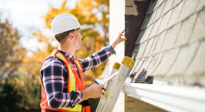 a man with hard hat standing on ladder inspecting roof