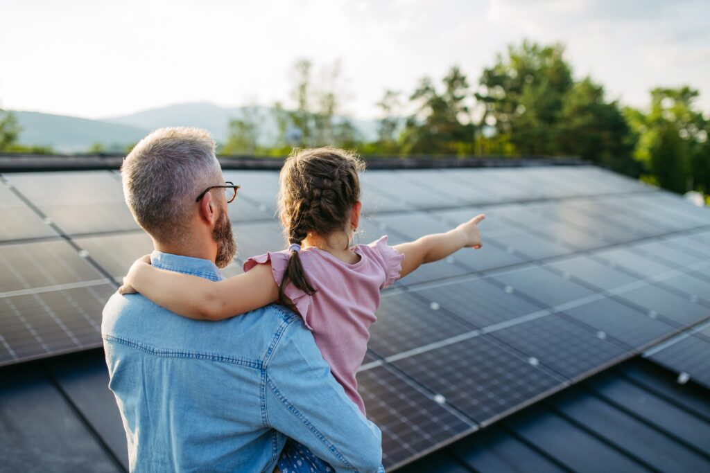 dad carrying little girl pointing at solar on roof