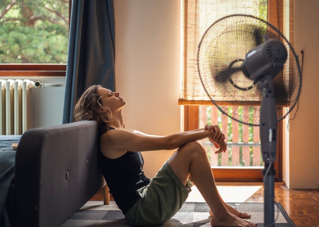 young woman suffering from heat sitting on floor of home with fan
