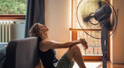 young woman suffering from heat sitting on floor of home with fan