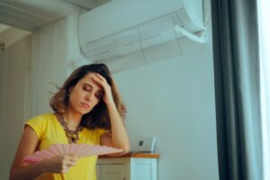 woman using a hand fan with a broken air conditioner