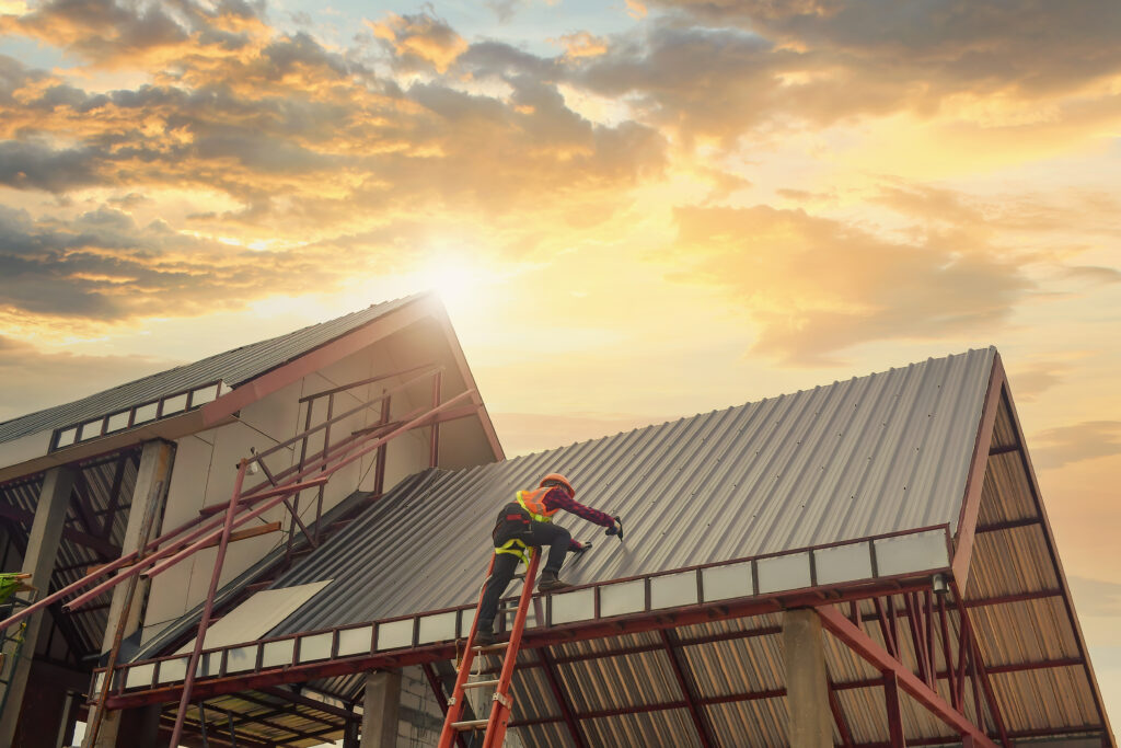 construction worker on ladder working on roof during sunset