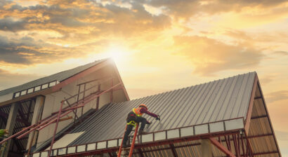 construction worker on ladder working on roof during sunset