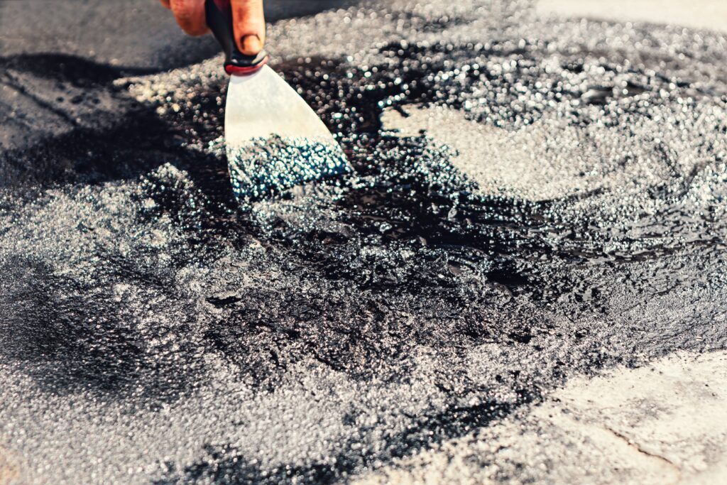 person using putty knife to spread thick black tar