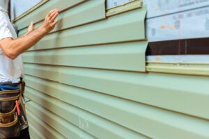 construction worker installs green siding boards