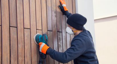 man in mask sanding siding on a home