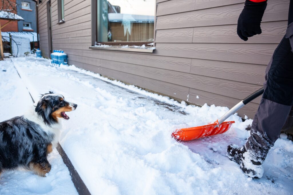 person uses an orange snow shovel outside of snowy home