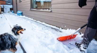person uses an orange snow shovel outside of snowy home