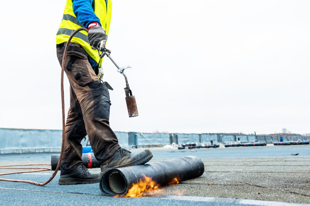 worker in vest using a torch for roofing