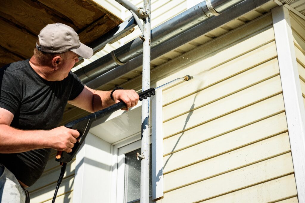 man washing the vinyl siding wall of home