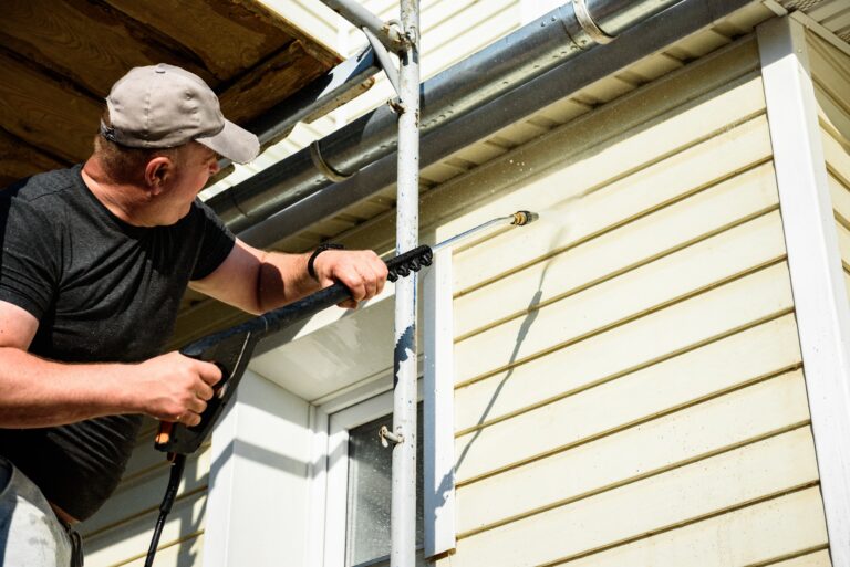man washing the vinyl siding wall of home